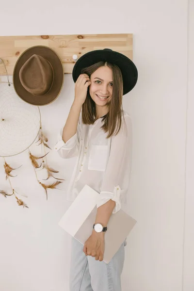 A beautiful smiling girl in a black hat is looking into the camera and smiling. Summer beauty. Romantic shot. Hats on the background — Stock Photo, Image