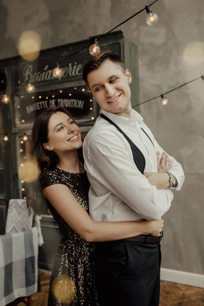 Dulce pareja está en el fondo café francés. Chica está en vestido de purpurina abraza a su novio. Luces. Estilo. Amor. —  Fotos de Stock