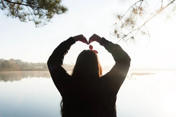 Silhouette of Woman\'s hands forming a heart shape on morning sunrise.