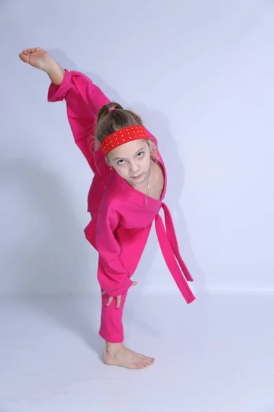 Pembe kimono küçük kız beyaz arka plan üzerinde egzersizler yapıyor