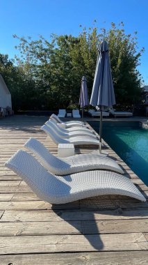 Otel havuzunun yanındaki güneş pansiyonları. Yüzme havuzunun yanında boş güneş pansiyonları. Beyaz plastik güneş pansiyonları açık mavi yüzme havuzunun yanındaki açık hava oteli avlusunda. Yaz tatili kavramı