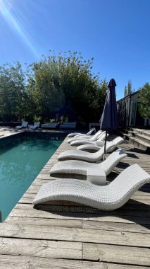 Otel havuzunun yanındaki güneş pansiyonları. Yüzme havuzunun yanında boş güneş pansiyonları. Beyaz plastik güneş pansiyonları açık mavi yüzme havuzunun yanındaki açık hava oteli avlusunda. Yaz tatili kavramı