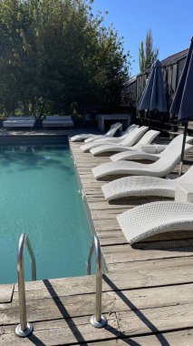 Otel havuzunun yanındaki güneş pansiyonları. Yüzme havuzunun yanında boş güneş pansiyonları. Beyaz plastik güneş pansiyonları açık mavi yüzme havuzunun yanındaki açık hava oteli avlusunda. Yaz tatili kavramı