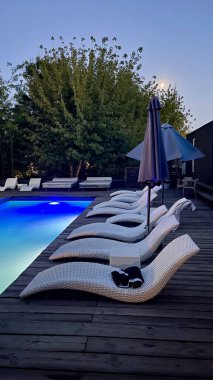 Otel havuzunun yanındaki güneş pansiyonları. Yüzme havuzunun yanında boş güneş pansiyonları. Beyaz plastik güneş pansiyonları açık mavi yüzme havuzunun yanındaki açık hava oteli avlusunda. Yaz tatili kavramı