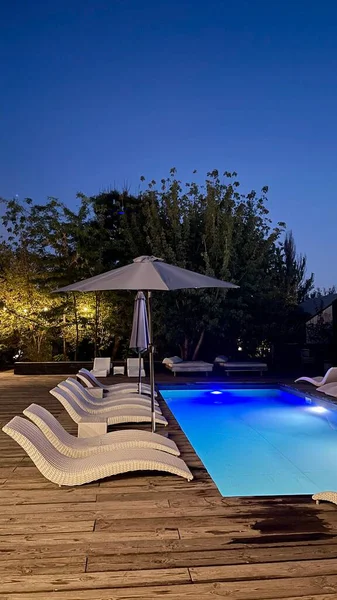 Otel havuzunun yanındaki güneş pansiyonları. Yüzme havuzunun yanında boş güneş pansiyonları. Beyaz plastik güneş pansiyonları açık mavi yüzme havuzunun yanındaki açık hava oteli avlusunda. Yaz tatili kavramı