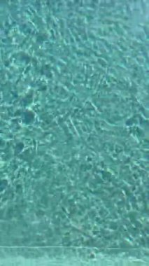 Yüzme havuzu yüzeyinde güneş ışığı yansıması olan dalgalı mavi suyun yakın görüntüsü. Mavi yüzme havuzu su yüzeyi ve dalgalı arka plan. Yüzme havuzu teması. Havuzda su yüzeyi