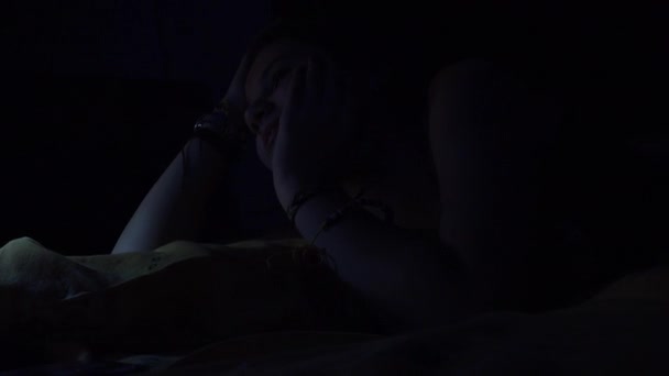 思春期の魅力的なスマート フォンを使用し 夜にベッドに横たわってリラックスし — ストック動画