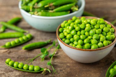 Ahşap zemin üzerinde yeşil bezelyeler olan taze bezelye kabukları. Tatlı yeşil bezelyeler. Yeşil bezelye fasulyesi sebzesi. Vejetaryen. Sağlıklı sebze. Boşluğu kopyala