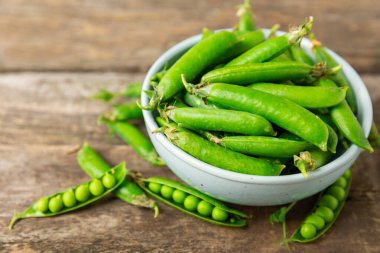 Ahşap zemin üzerinde yeşil bezelyeler olan taze bezelye kabukları. Tatlı yeşil bezelyeler. Yeşil bezelye fasulyesi sebzesi. Vejetaryen. Sağlıklı sebze. Boşluğu kopyala