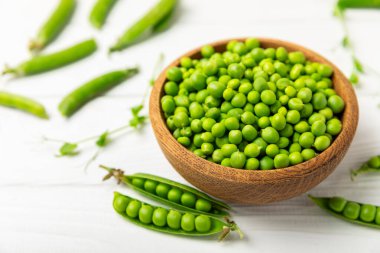 Ahşap zemin üzerinde yeşil bezelyeler olan taze bezelye kabukları. Tatlı yeşil bezelyeler. Yeşil bezelye fasulyesi sebzesi. Vejetaryen. Sağlıklı sebze. Boşluğu kopyala
