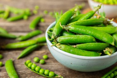 Ahşap zemin üzerinde yeşil bezelyeler olan taze bezelye kabukları. Tatlı yeşil bezelyeler. Yeşil bezelye fasulyesi sebzesi. Vejetaryen. Sağlıklı sebze. Boşluğu kopyala