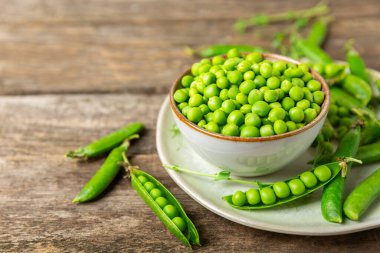 Ahşap zemin üzerinde yeşil bezelyeler olan taze bezelye kabukları. Tatlı yeşil bezelyeler. Yeşil bezelye fasulyesi sebzesi. Vejetaryen. Sağlıklı sebze. Boşluğu kopyala
