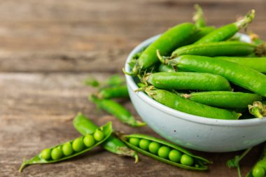 Ahşap zemin üzerinde yeşil bezelyeler olan taze bezelye kabukları. Tatlı yeşil bezelyeler. Yeşil bezelye fasulyesi sebzesi. Vejetaryen. Sağlıklı sebze. Boşluğu kopyala