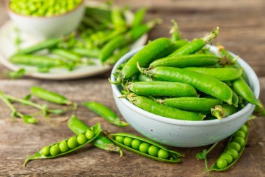 Ahşap zemin üzerinde yeşil bezelyeler olan taze bezelye kabukları. Tatlı yeşil bezelyeler. Yeşil bezelye fasulyesi sebzesi. Vejetaryen. Sağlıklı sebze. Boşluğu kopyala