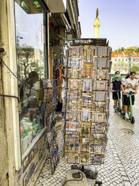Lizbon, Portekiz - Kartpostal gösterimi bir mağazanın dışında. Kartpostallar renkli ve çeşitli görüntüler içeriyor. Etrafta dolaşan birkaç kişi var, bazıları sırt çantası taşıyor.