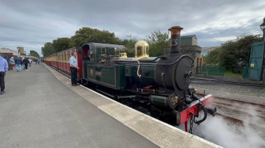 Douglas, Man Adası 08.05.2023 treni rayların üzerinde yanında bir adamla oturuyor. Tren yeşil ve kırmızı Man Adası -