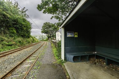 Laxey, Man Adası 08.05.2023 Yeşil bankı ve küçük bir barınağı olan tren istasyonu. Yedek kulübesi boş. Sığınak yeşil ve üzerinde bir işaret var. Tren rayları arka planda Man Adası 'nda. -