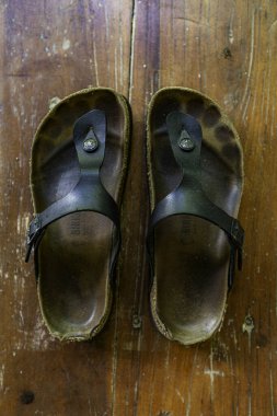 Kahverengi tabanlı bir çift siyah sandalet. Sandaletler yıpranmış ve yıpranmış görünüyor.