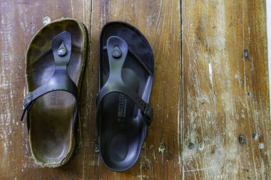 İki parmak arası terlik, biri siyah, diğeri kahverengi. Siyah olan yıpranmış ve yıpranmış görünüyor.