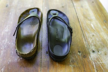 İki parmak arası terlik, biri siyah, diğeri kahverengi. Siyah parmak arası terliğin siyah bir kayışı ve siyah tabanı var.