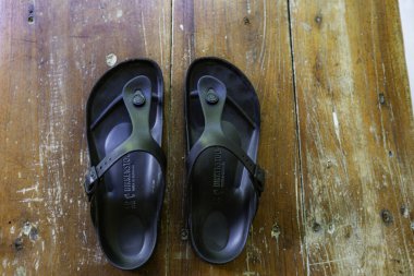 İki siyah Birkenstock sandaleti ahşap bir masanın üzerinde yatıyor. Sandaletler siyah ve siyah bir kayışı var.