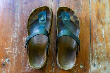 Kahverengi tabanlı ve siyah kayışlı iki siyah sandalet. Sandaletler yıpranmış ve kirli.