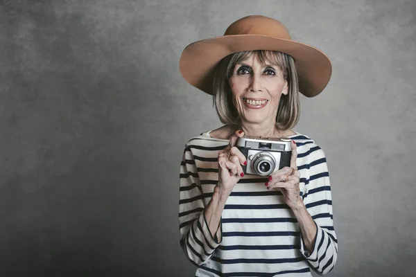 Portrait of Smiling senior woman with vintage photo camera on gray background