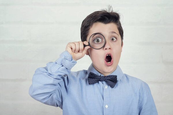 surprised child looking through magnifying glass on brick background