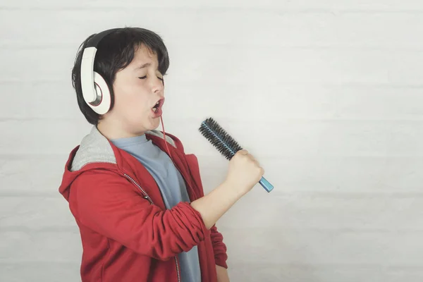 Roligt barn i hörlurar sjunga med hårborste — Stockfoto