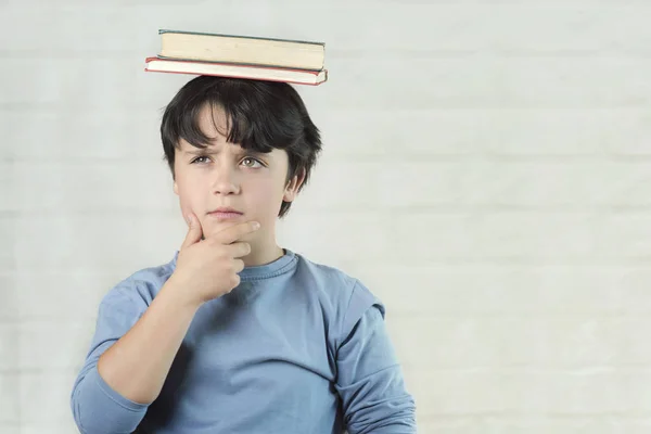 Niño reflexivo con libros en la cabeza — Foto de Stock