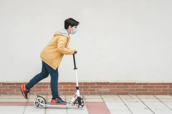 happy kid wearing medical mask with his scooter in the city outdoors