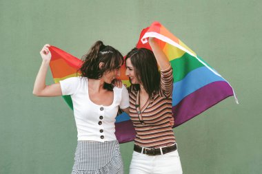 Genç bayan arkadaşlar yeşil arka planda LGBT bayrağı sallıyorlar.