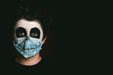 Cadılar Bayramı 'nız kutlu olsun. Siyah arka planda, iskelet kostümlü, tıbbi maske takan bir çocuğun yakın çekimi.