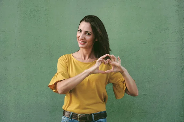 smiling young woman showing heart with hands over green background