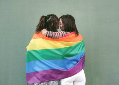 Genç bayan arkadaşlar yeşil arka planda LGBT bayrağı sallıyorlar.