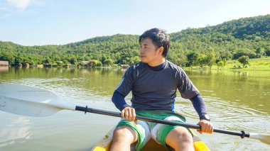 Genç adam kanoyla nehirde oturuyor.