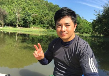 Arka planda yeşil nehir olan barış işareti gösteren genç bir adam.