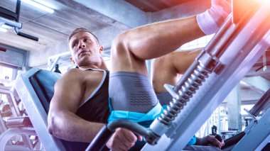 spor salonunda makinede genç adam egzersiz bacak