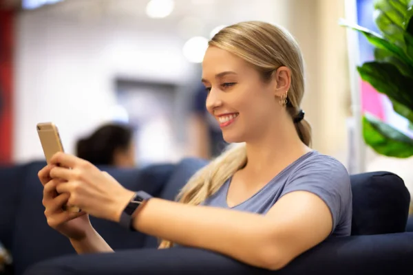 side view of women looking on mobile phone with smiling while sitting on sofa