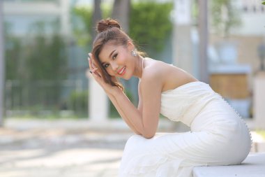 Parkta oturan beyaz gelinlik içinde uzun etekli güzel bir gelinin portresi. Kopyalama alanı olan kenar görünümü.