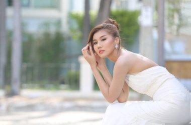 Parkta oturan beyaz gelinlik içinde uzun etekli güzel bir gelinin portresi. Kopyalama alanı olan kenar görünümü.