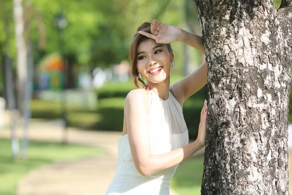 美丽迷人的新娘穿着婚纱 长长的长裙 站在公园的一棵树旁 — 图库照片