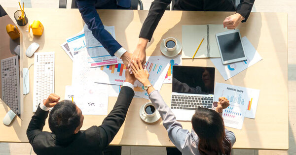 Business Team Stacking Hands At Conference Table. High angle view of business team stacking hands at conference table in board room. Horizontal shot.