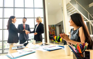 Genç iş adamları ofiste birlikte çalışıyorlar. Yönetici bir tabloya işaret ediyor ve iş stratejileri hakkındaki analizleri açıklıyor. İş dünyasının en iyi el sıkışması.