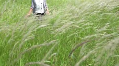 Kadın elini çimenlerin üzerinden geçirir ve tarlada yürürken ona dokunur. 