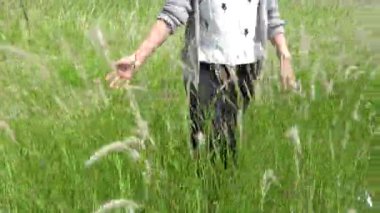 Kadın elini çimenlerin üzerinden geçirir ve tarlada yürürken ona dokunur. 