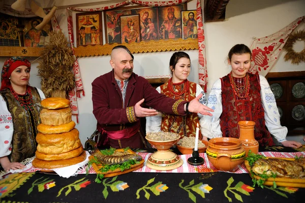 Ukrayna yerlisi elbiseli aile Noel arifesini kutlamak için geleneksel tabaklarla masanın arkasında duruyor.