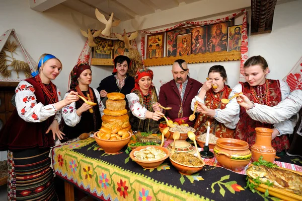 Ukrayna yerlisi elbiseli aile Noel arifesini kutlamak için geleneksel tabaklarla masanın arkasında duruyor.