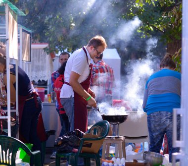 Erkek aşçı açık ateşte yemek hazırlıyor tezgahın arkasındaki tezgahta sokak yemeği satıyor. 3 Haziran 2018. Kiev, Ukrayna