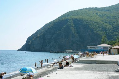 Gurzuf şehrinin taşlı plajını, güneşlenmeye ve yüzmeye gidenleri, arka planda dağları görmek. 10 Haziran 2017. Gurzuf, Kırım